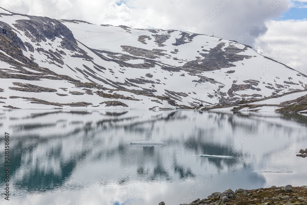 snow mountains surrounded by clouds in norwegian fiord reflection in water, selective focus