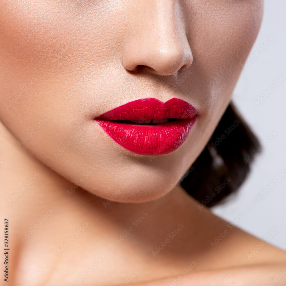 Fototapeta premium Photo of closeup of a part of a woman's face. Lips of a beautiful girl with bright red lipstick. Macro image of the girl's lips painted with red lipstick.