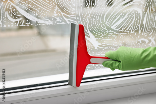 Woman cleaning window with squeegee indoors, closeup