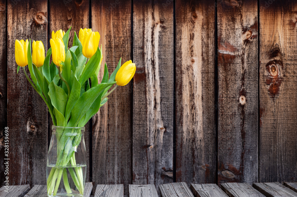 Fototapeta Wiązanka żółtych wiosennych tulipanów w szklanym pojemniku na nieociosanych deskach