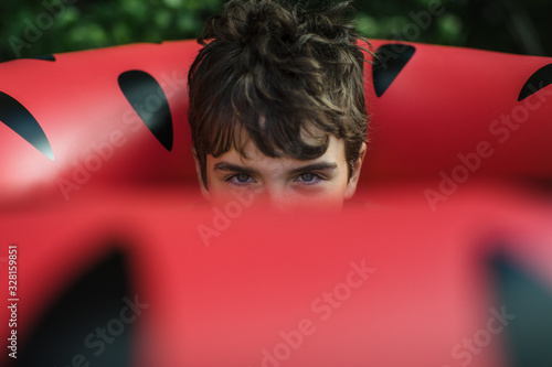 Boy peers out from hole in watermelon float on summer beach vacation photo