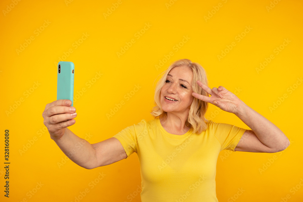 Handsome blond adult woman making self photo in the bright yellow studio Handsome blond adult woman making self photo in the bright yellow studio