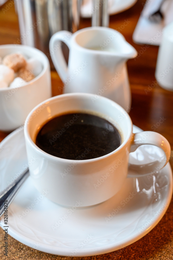 White cup with black coffee and hot milk jug White cup with black coffee and hot milk jug