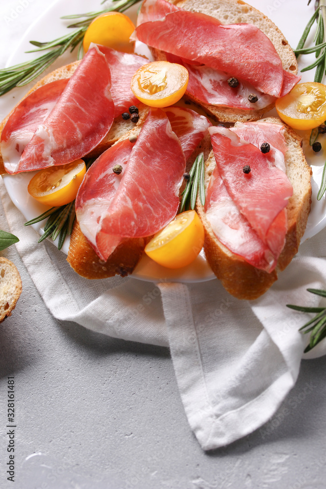 The concept of Italian cuisine. Coppa - Italian dried sausage made from pork neck. Meat snacks. Baguette, cherry tomatoes, rosemary on a light white background. Background image, copy space The concept of Italian cuisine. Coppa - Italian dried sausage made from pork neck. Meat snacks. Baguette, cherry tomatoes, rosemary on a light white background. Background image, copy space