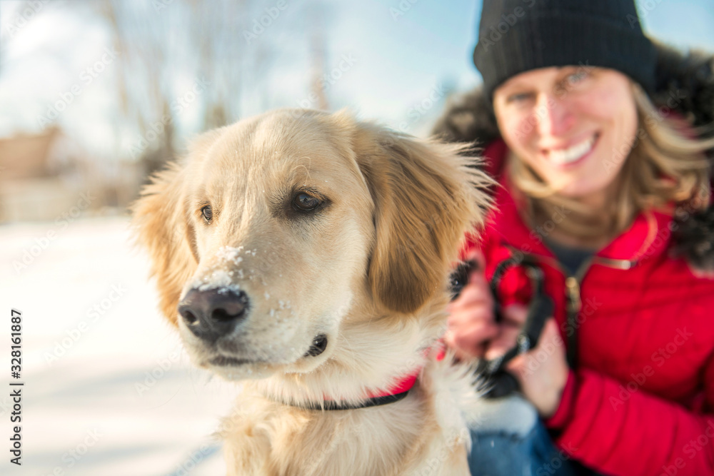 Attractive mid adult blond woman in snow with Golden Retriever.