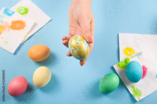 A female hand holds only a painted Easter egg among other painted eggs on a blue background.