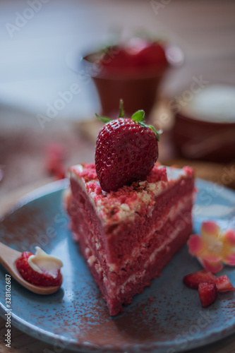 Close-up of a Red Velvet cake on a blue plate with strawberries and pure cocoa with a rustic background with flowers and cloth napkins