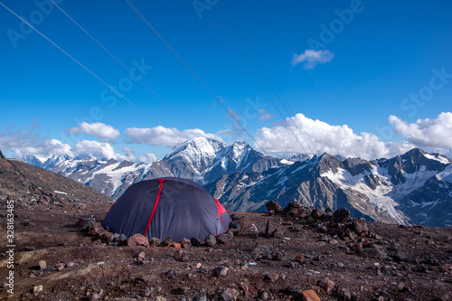 Close up of expedition tent, secured with rocks. Mount Elbrus, Caucasus, Russia. Accommodation in mountains. Sky and white clouds in the backkround. Back View.