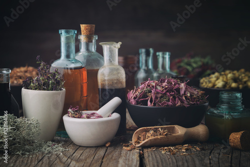 Bottles of healthy tincture or infusion, mortar and bowls of medicinal herbs on table. Herbal medicine.