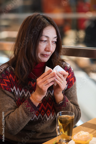 Nice Asian young woman wiping her nose and having a cup of tea after shopping in a cafe