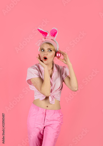 Surprised woman in rabbit bunny ears holds pink egg. Happy Easter. Hunt for Easter eggs. Hunting eggs. Blonde girl with color egg. Spring holiday. Happy woman preparing for Easter. Easter celebration.