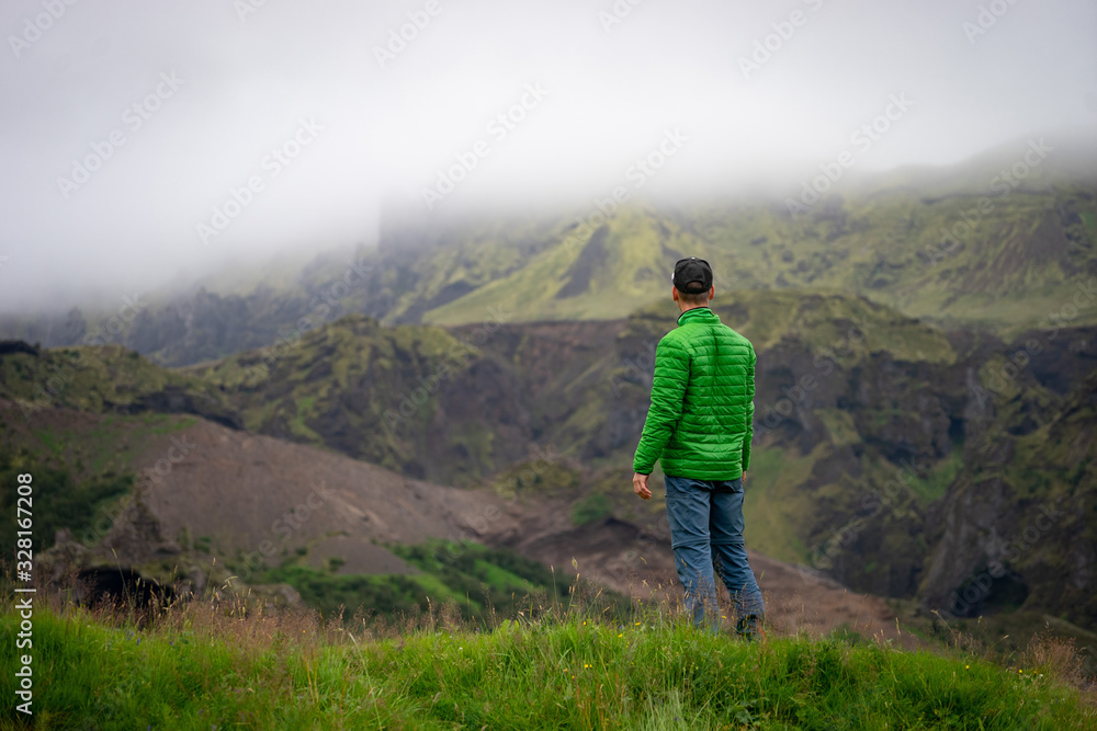 Backside of tall caucasian man wearing green jacket standing in over mountain and fog background. Promoting healthy lifestyle
