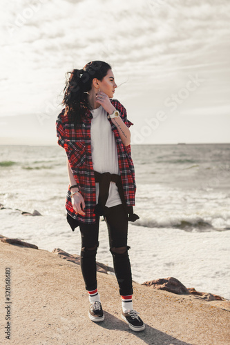 Young happy girl in red wearing a checkered shirt walks on the beach. Wide-open shirt. Awesome atmosphere  Spring time.