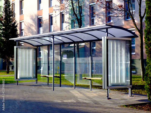 clear glass and aluminum frame structure bus shelter at bus stop in residential area. bare trees and green grass in the background. public transportation. ad and copy space. photo