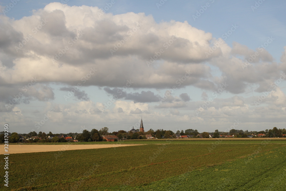 Obraz premium a landscape in the dutch countryside in springtime with a little village with a church behind the fields with growing green crops and a blue sky with big white clouds