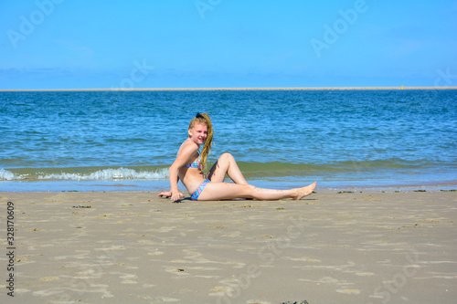 Young girl in bikini on the sand beach in front of the sea