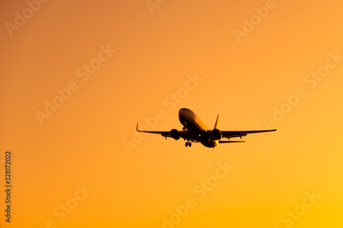 Large airliner passengers view is landing on the landing strip at the airport against the backdrop of bright orange sunset on a sunny summer day. A plane flies in the sky at sunset day
