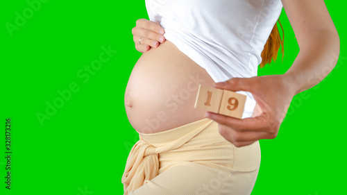 A happy pregnant young woman holding wooden cubes with 19 numbers next to her belly. Photos of belly growth at 19 weeks pregnancy. Healthy pregnancy diet and fetal development. photo