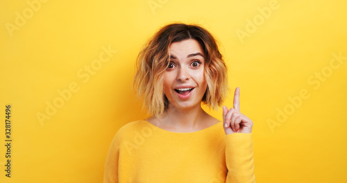Bilde på lerret Portrait happy young woman slow motion of finding solution Idea pointing forward an index finger on isolated yellow background, looking directly at the camera smiling