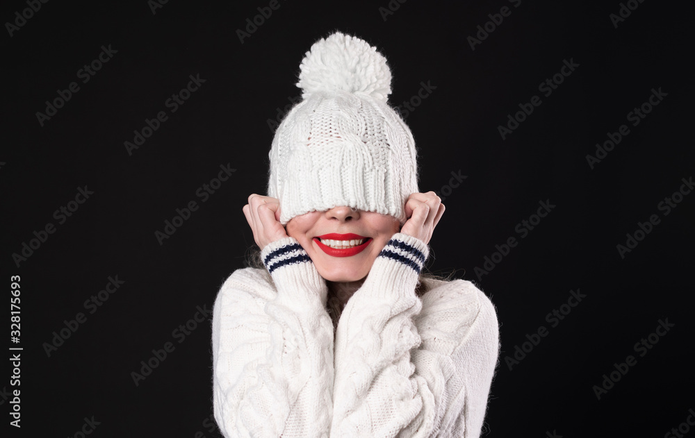 Beautiful young happy smiling girl hiding her eyes under trendy white big loop knitted beanie hat. Model wearing winter sweater. Close up Beautiful young happy smiling girl hiding her eyes under trendy white big loop knitted beanie hat. Model wearing winter sweater. Close up
