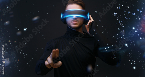Guy using VR helmet scrolling invisible screen while interacting with virtual reality under blue neon light. Augmented reality, future technology, game concept.