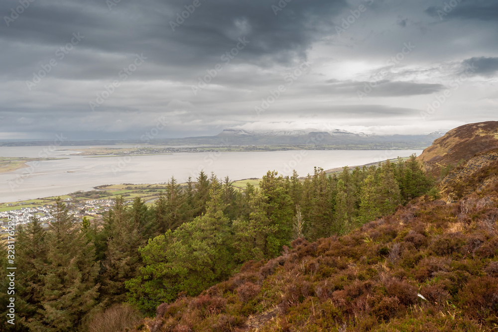 Beautiful view from Knocknarea hill on Creggconnell and Benbulben flat top mountain covered with snow and clouds, County Sligo. Dramatic cloudy sky.