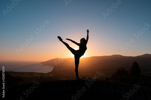 Silhouette of woman dancing at sunset with mountains and sea on background