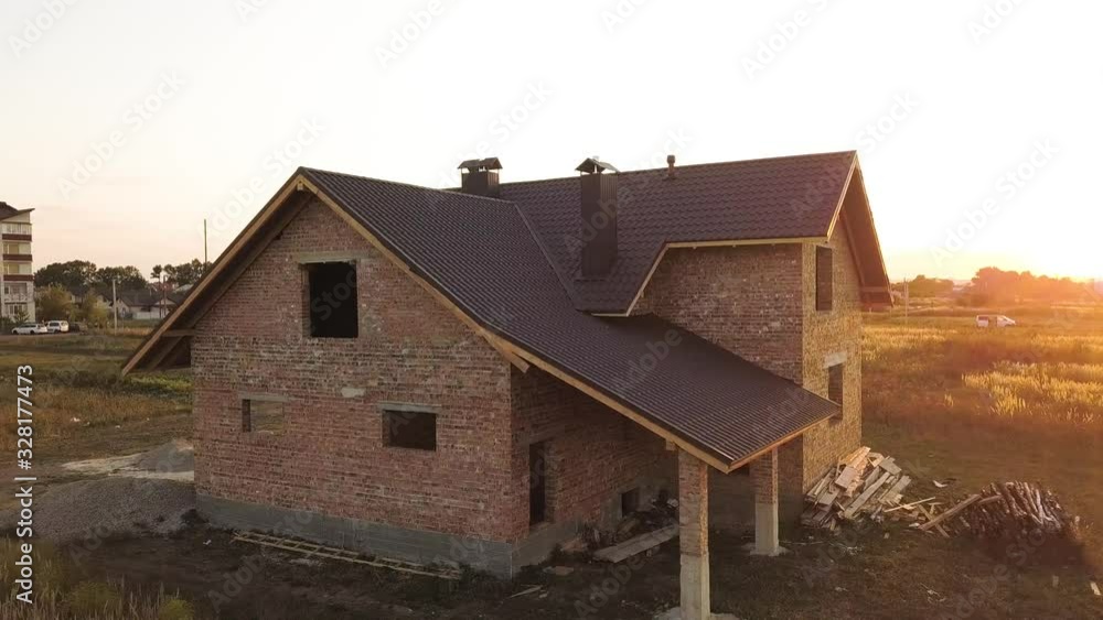 Aerial view of unfinished house with wooden roof structure covered with metal tile sheets under construction. Aerial view of unfinished house with wooden roof structure covered with metal tile sheets under construction.