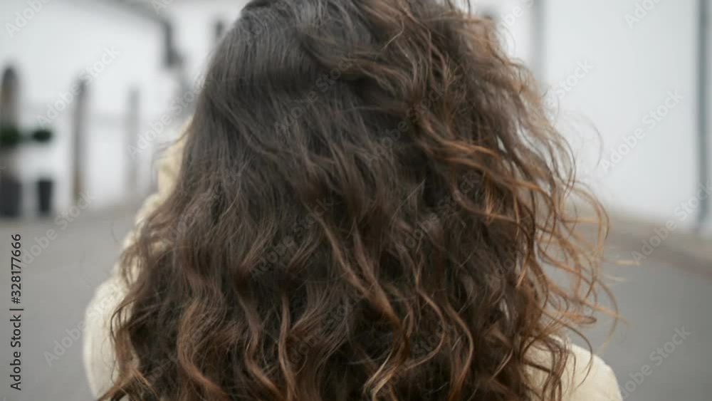 A Girl brown-haired woman with long curly hair walks down the street looking with a back slow motion A Girl brown-haired woman with long curly hair walks down the street looking with a back slow motion