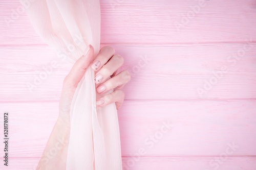 Beautiful female hand holding flowing silk fabric. Natural manicure with pink color nail polish, black flowers pattern. Pale pink background. Copy space © kvitkanastroyu