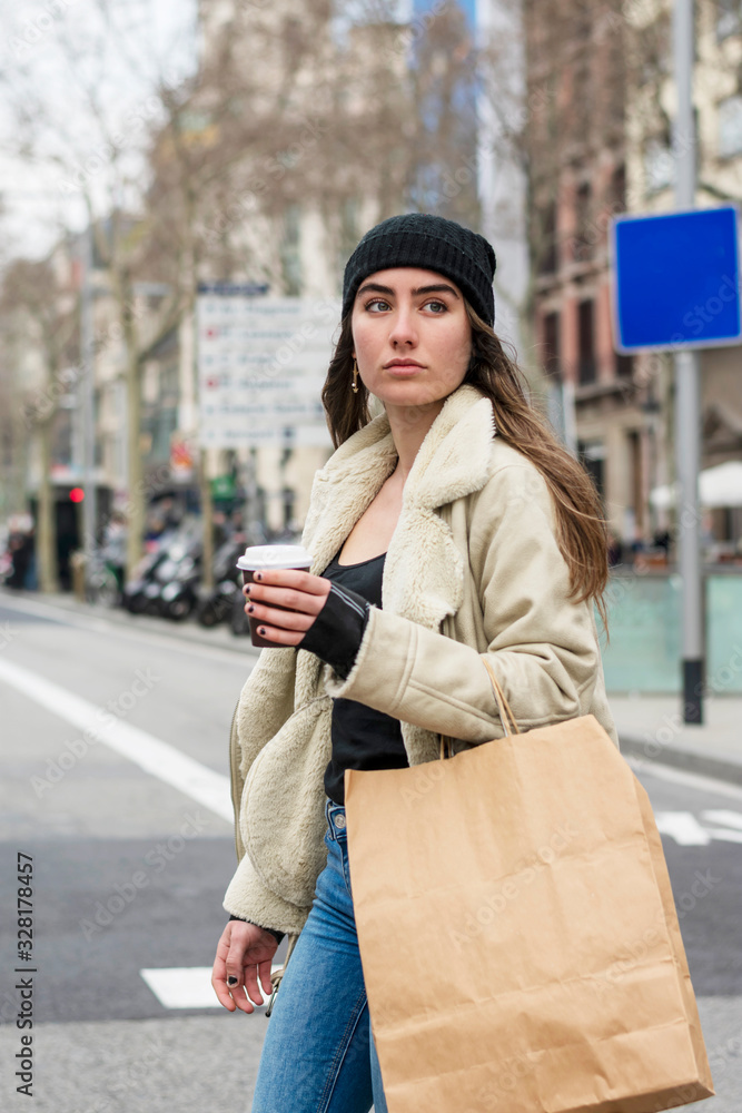 Fototapeta premium Portrait of young european woman walking in a city street, with takeaway coffee in hands