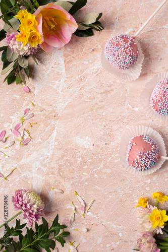 Spring frame copy space from early spring flowers and bright pink cake pops on a pink marble background.