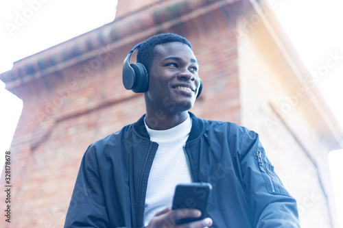 Fotografi Young Black man standing in the street while listening music by headphones