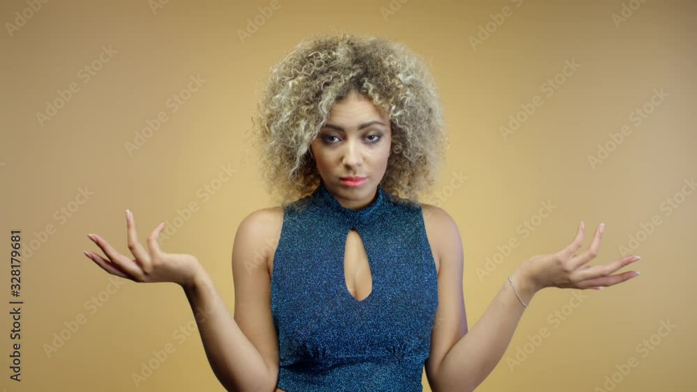 Angry puzzled young mixed race woman in blue shiny blouse spreads her hands to sides standing on yellow background. Languishing look. Disappointed hispanic girl looking at camera gesturing with hands Angry puzzled young mixed race woman in blue shiny blouse spreads her hands to sides standing on yellow background. Languishing look. Disappointed hispanic girl looking at camera gesturing with hands