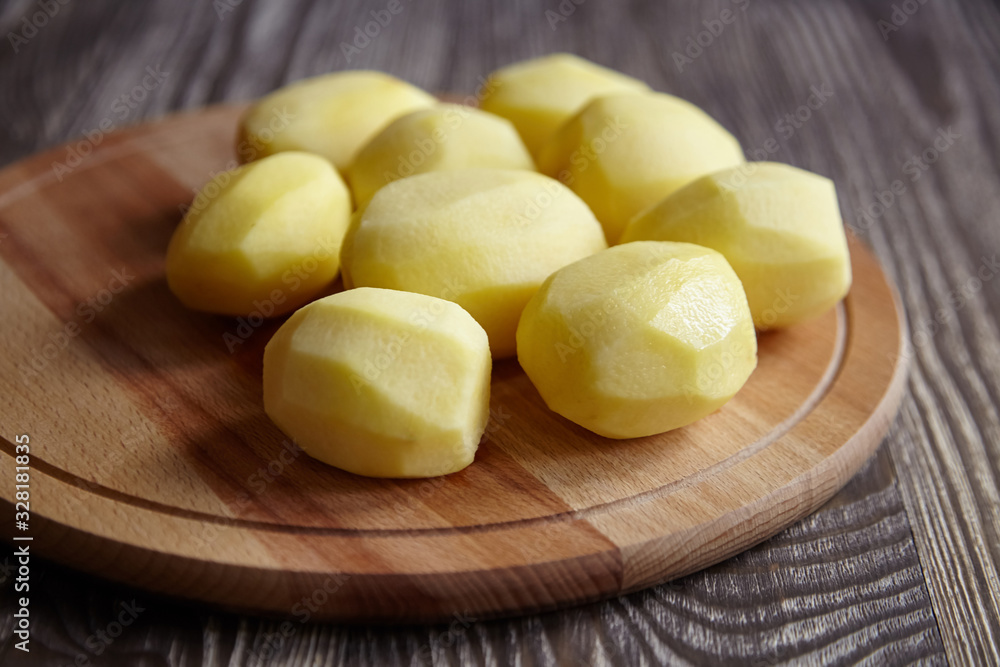 Peeled potatoes on wooden cutting board on brown table Peeled potatoes on wooden cutting board on brown table