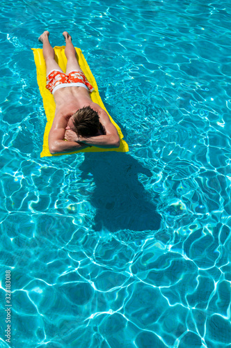 Unrecognizable man in colorful swim shorts floating on an inflatable lilo on a bright blue swimming pool