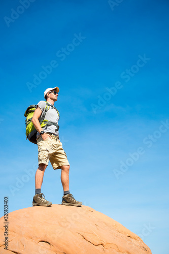 Hiker standing outdoors on the top of a red rock mountain under sunny blue sky