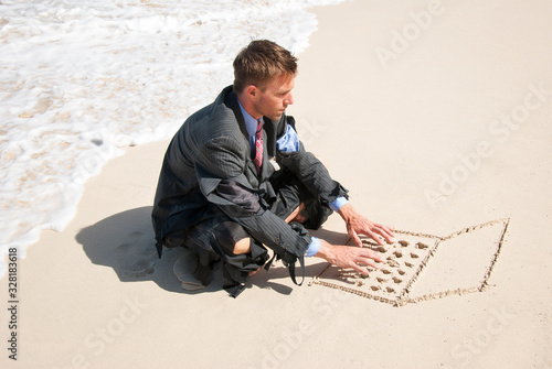 Businessman working on his sand laptop next to foamy white waves washing up the beach