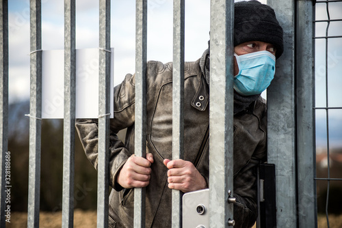 Portrait of man with medical mask to protect against the corona virus opening the metallic fence