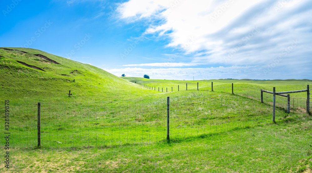 Mesh farm fence dividing beautiful green hills and meadows under blue sky with white clouds in Australia