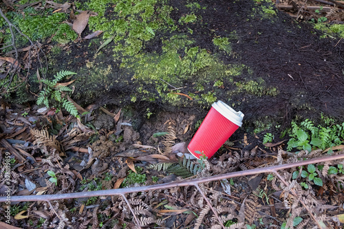 Red disposable coffee cup lying on the forest ground - ecology concept