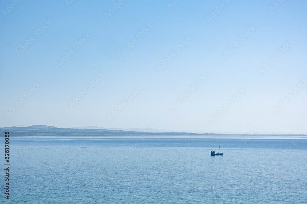 Minimalist landscape - lonely fishing boat in the vast ocean in bright sunlight under blue sky with copy space