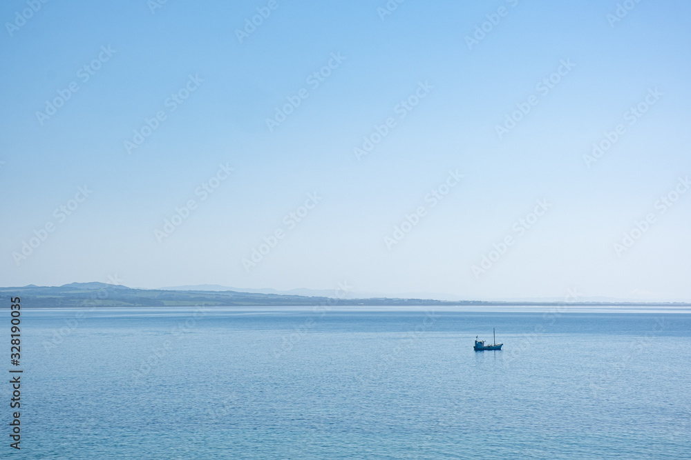 Minimalist landscape - lonely fishing boat in the vast ocean in bright sunlight under blue sky with copy space Minimalist landscape - lonely fishing boat in the vast ocean in bright sunlight under blue sky with copy space