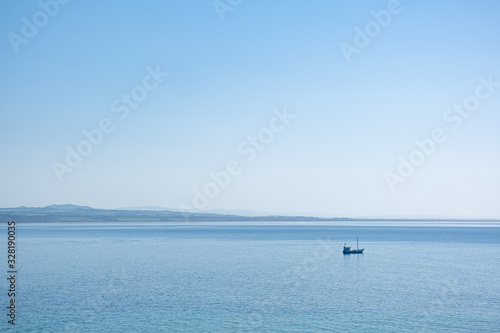 Minimalist landscape - lonely fishing boat in the vast ocean in bright sunlight under blue sky with copy space