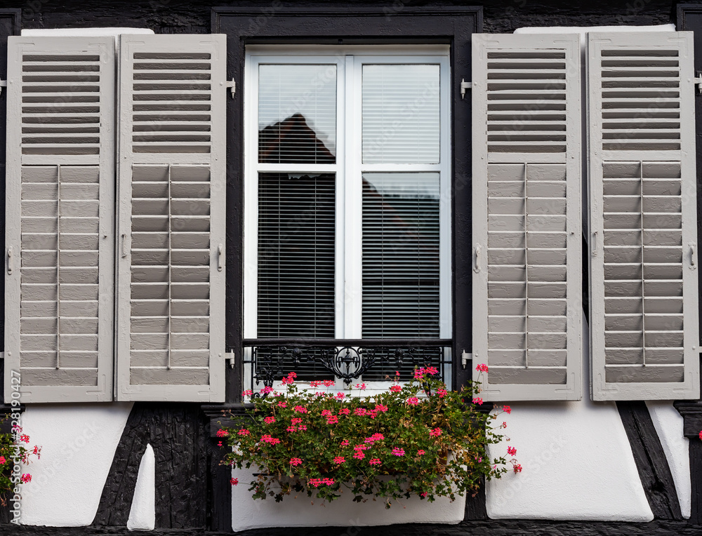 Classic Alsatian windows in a half-timbered house, decorated with wooden carvings and flowers Classic Alsatian windows in a half-timbered house, decorated with wooden carvings and flowers