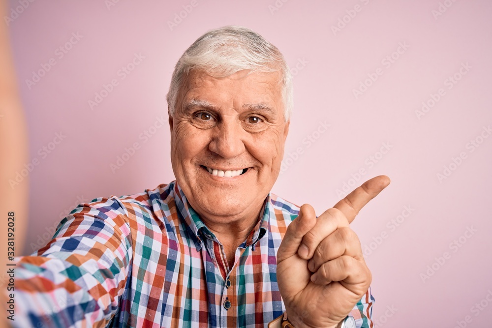 Senior handsome hoary man wearing casual shirt making selfie by the camera very happy pointing with hand and finger to the side Senior handsome hoary man wearing casual shirt making selfie by the camera very happy pointing with hand and finger to the side
