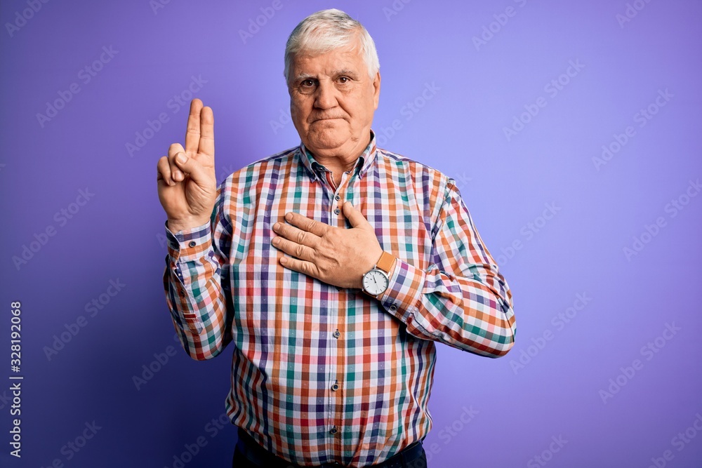 Fototapeta premium Senior handsome hoary man wearing casual colorful shirt over isolated purple background smiling swearing with hand on chest and fingers up, making a loyalty promise oath