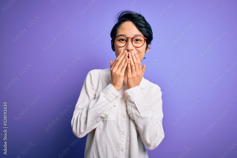 Young beautiful asian girl wearing casual shirt and glasses standing over purple background laughing and embarrassed giggle covering mouth with hands, gossip and scandal concept Young beautiful asian girl wearing casual shirt and glasses standing over purple background laughing and embarrassed giggle covering mouth with hands, gossip and scandal concept