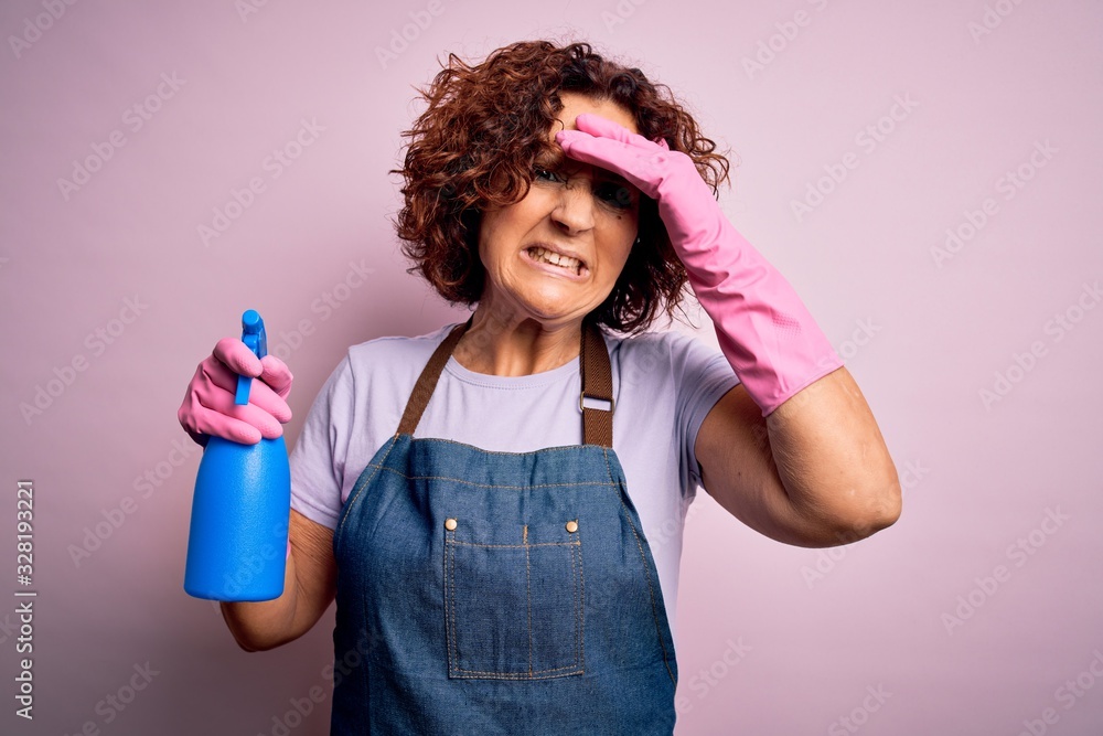 Middle age curly hair woman cleaning doing housework wearing apron and gloves using spayer stressed with hand on head, shocked with shame and surprise face, angry and frustrated. Fear and upset Middle age curly hair woman cleaning doing housework wearing apron and gloves using spayer stressed with hand on head, shocked with shame and surprise face, angry and frustrated. Fear and upset
