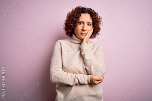 Middle age beautiful curly hair woman wearing casual turtleneck sweater over pink background thinking looking tired and bored with depression problems with crossed arms.